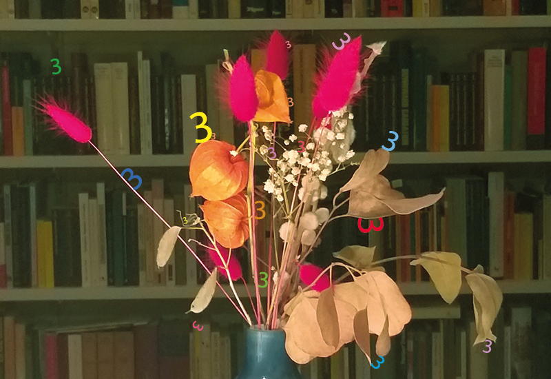 Papierblumen mit lauter kleinen Ziffern der 3 vor einem Bücherregal